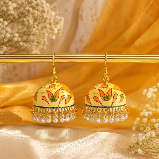 Ivory dome-shaped jhumka earrings with orange lotus floral design and pearl bead drops. Traditional handcrafted earrings displayed on a wooden surface with a handwritten tag.