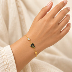 "Gold-tone chain bracelet
featuring a small black heart-shaped charm, an adjustable chain extension, and a delicate heart-shaped end charm, worn on a wrist."