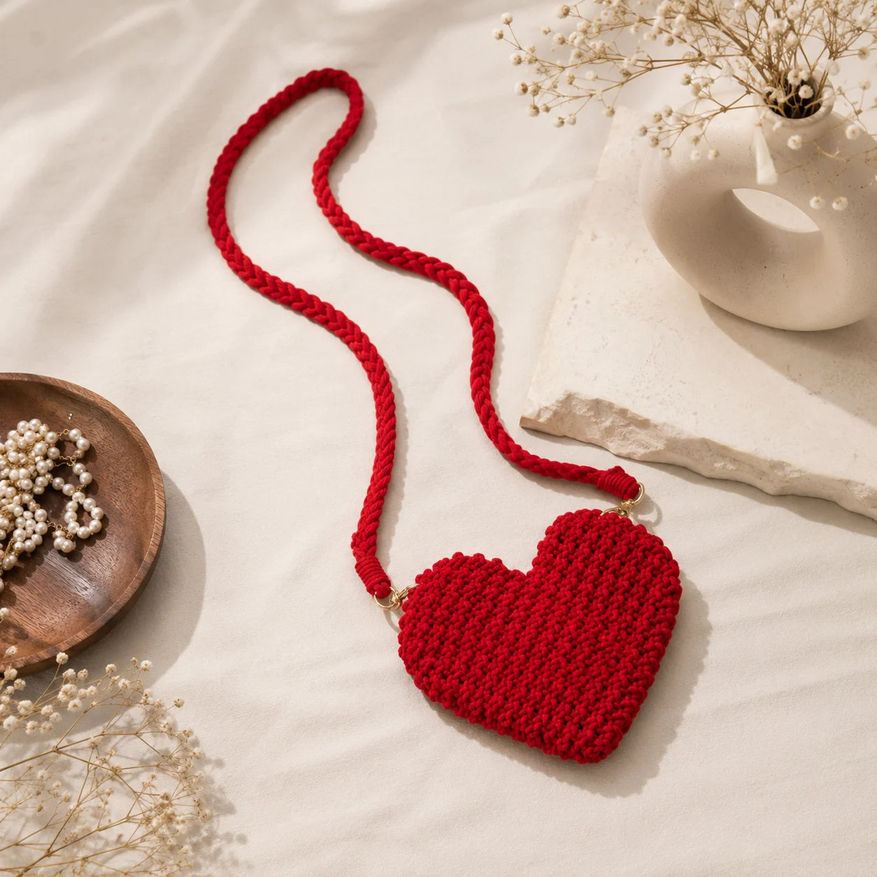 Red handwoven macrame heart-shaped sling bag with open-knit pattern and scalloped edge. Features braided rope strap with gold-tone lobster clasps. Boho cotton heart bag for daily and gifting.