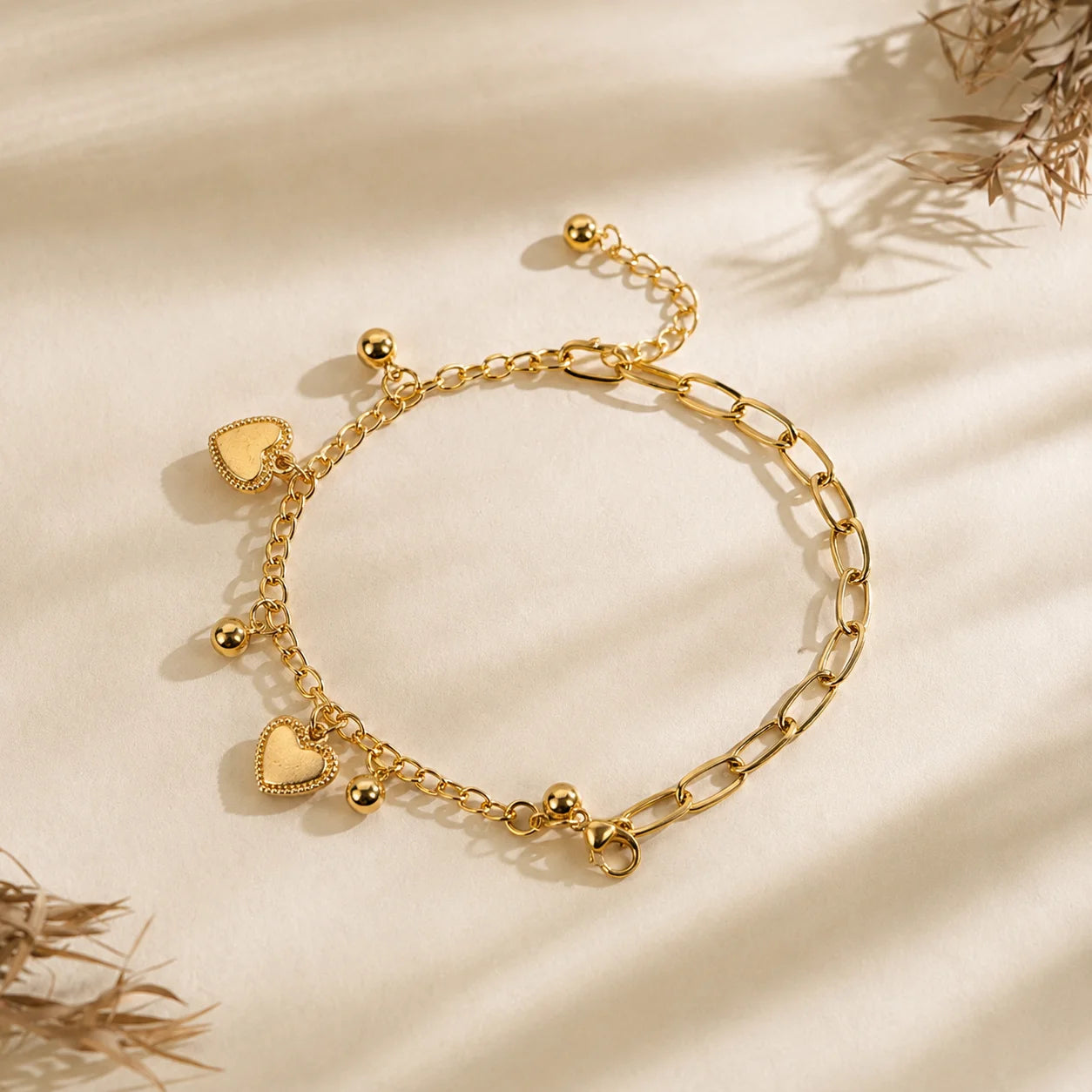 Gold-tone double layer chain bracelet with two white enamel heart charms. Accented with small ball bead dangles on mixed link chains with extender. Western charm bracelet displayed on wooden surface.