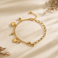 Gold-tone double layer chain bracelet with two white enamel heart charms. Accented with small ball bead dangles on mixed link chains with extender. Western charm bracelet displayed on wooden surface.