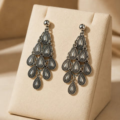 Antique silver chandelier dangle earrings with tiered teardrop motifs on wood surface. Ethnic fusion raindrop chandelier earrings with antique finish and push back post for women.