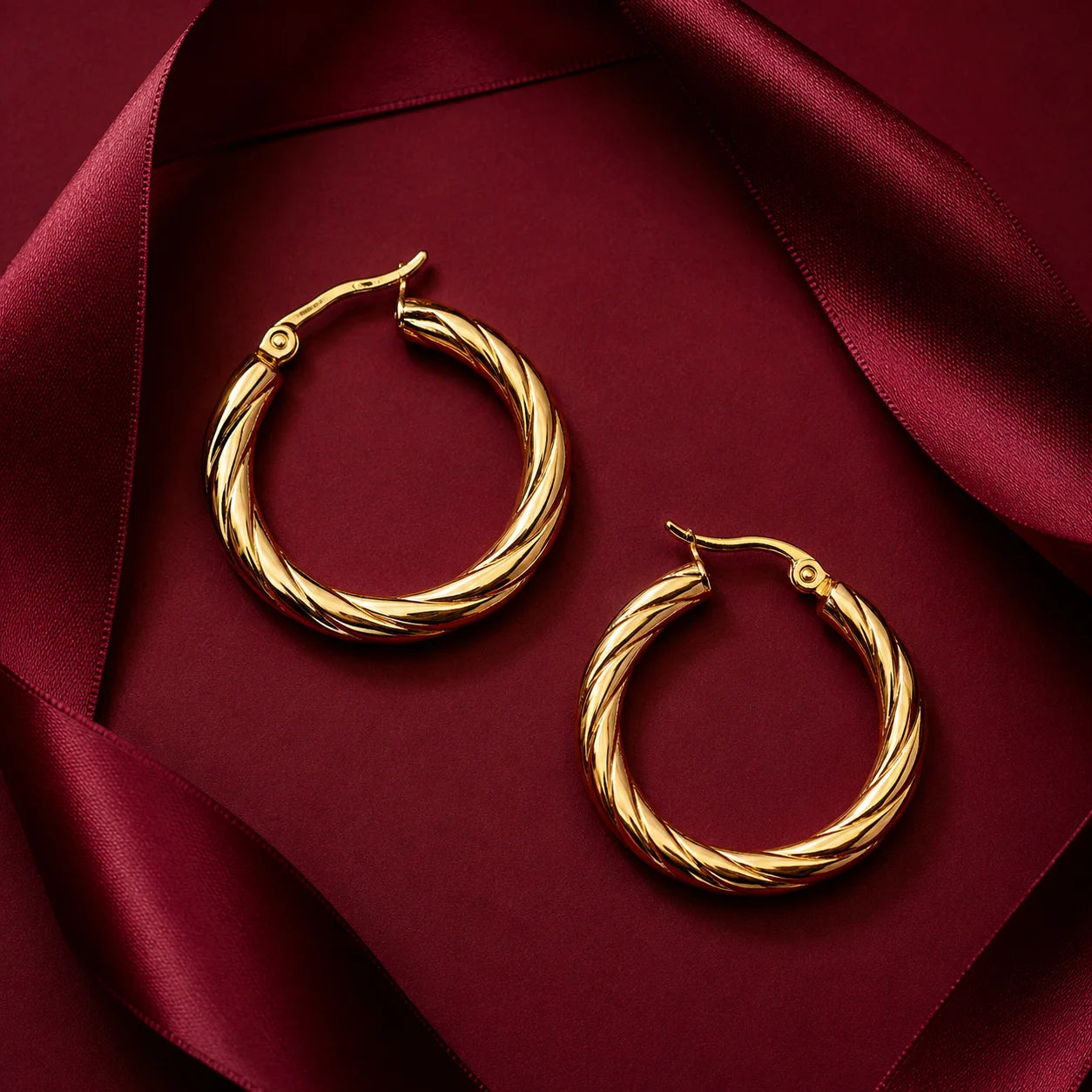 Pair of gold twisted hoop earrings with hinged closure on wooden table. Medium size gold-tone hoops with diagonal rope texture design.