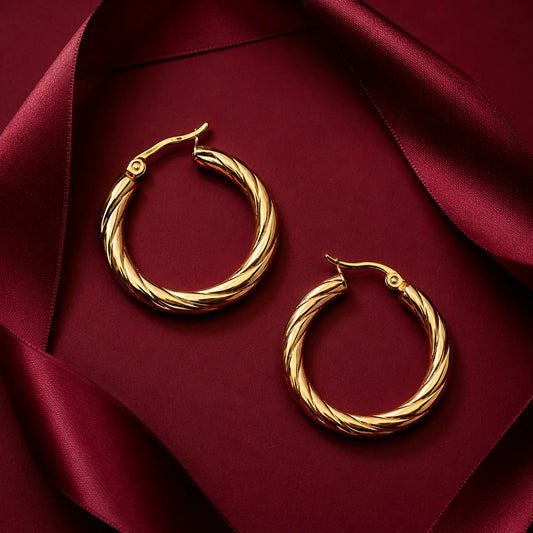 Pair of gold twisted hoop earrings with hinged closure on wooden table. Medium size gold-tone hoops with diagonal rope texture design.