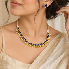 Blue kundan square necklace set with gold-toned detailing, dangling gold beads, and matching blue stone earrings.