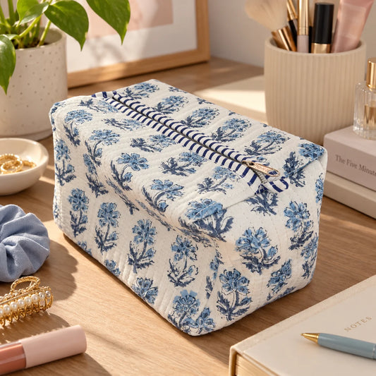"Quilted white pouch
with an intricate blue floral print and striped trim detail, photographed on a wooden table."