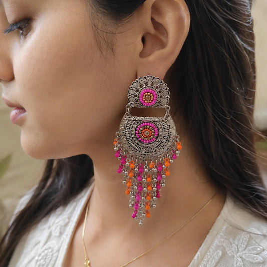 "Oxidised silver-tone earrings
with intricate engraved detailing, vibrant pink and orange bead accents, and cascading metallic tassels. Boho ethnic earrings for women, perfect for Navratri, festive celebrations, weddings, cultural events, and Indo-western styling."