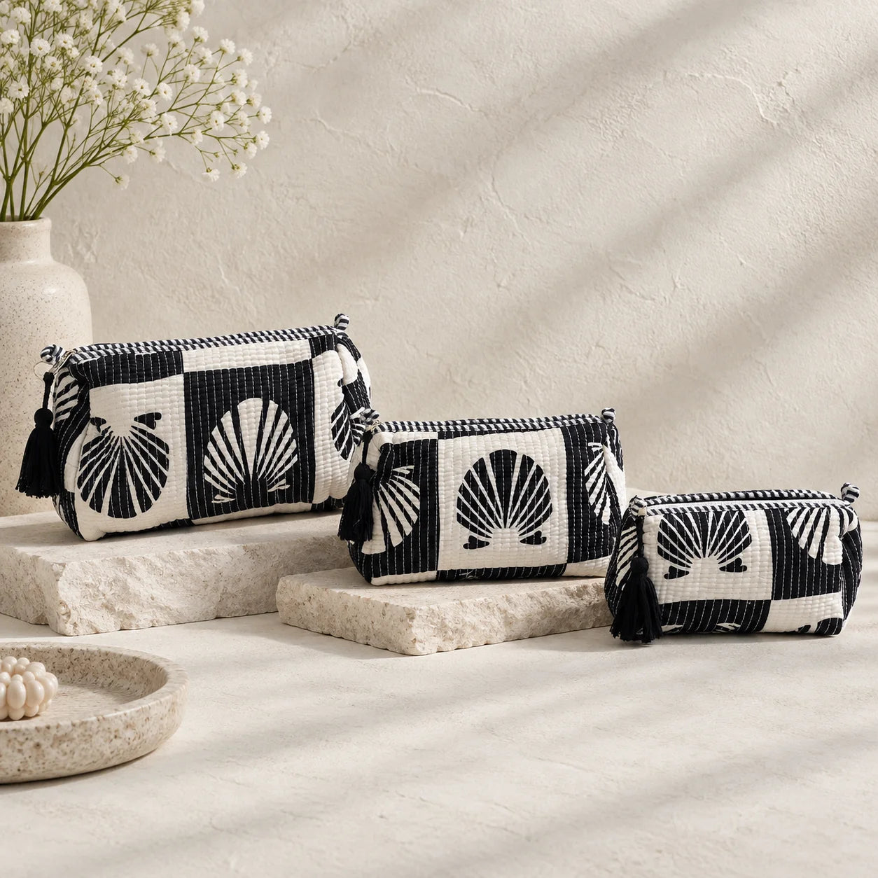 Set of three black and white quilted cotton travel pouches with bold shell fan block print and black tassel zippers stacked