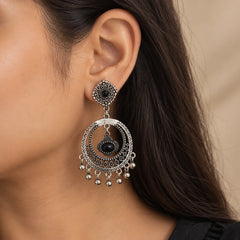 "Pair of oxidised silver-tone
earrings featuring intricate floral and geometric patterns, large circular drops, central hanging charms, and tiny silver bead accents."