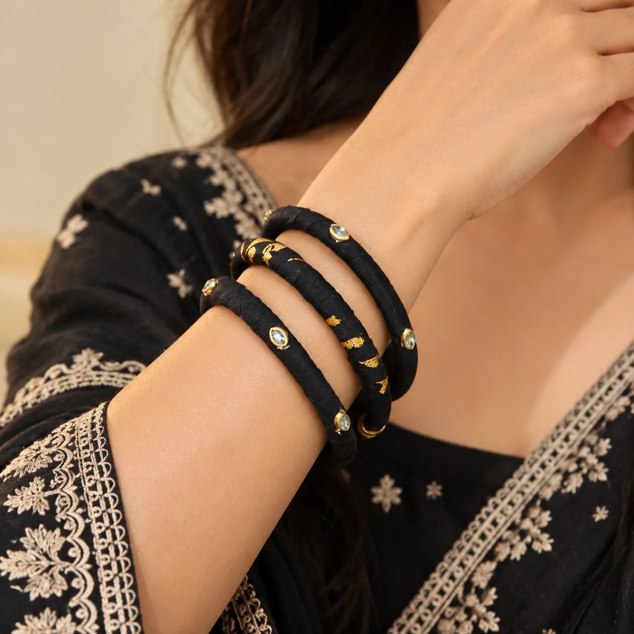 "Black fabric-wrapped
bangle set featuring gold-tone accents, delicate stone embellishments, and a mix of solid black and gold-printed designs."