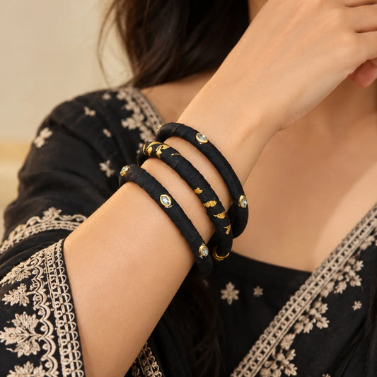 "Black fabric-wrapped
bangle set featuring gold-tone accents, delicate stone embellishments, and a mix of solid black and gold-printed designs."