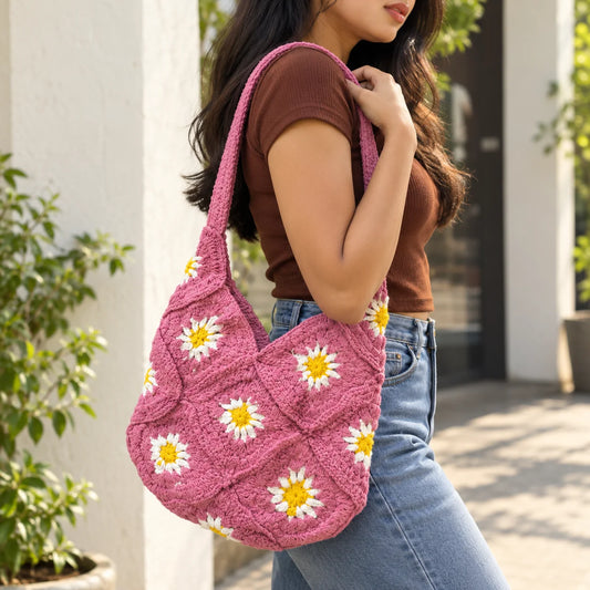 "Dusty pink crochet
shoulder bag featuring white daisy flowers with yellow centres, a textured granny-square pattern, and a matching crochet strap."