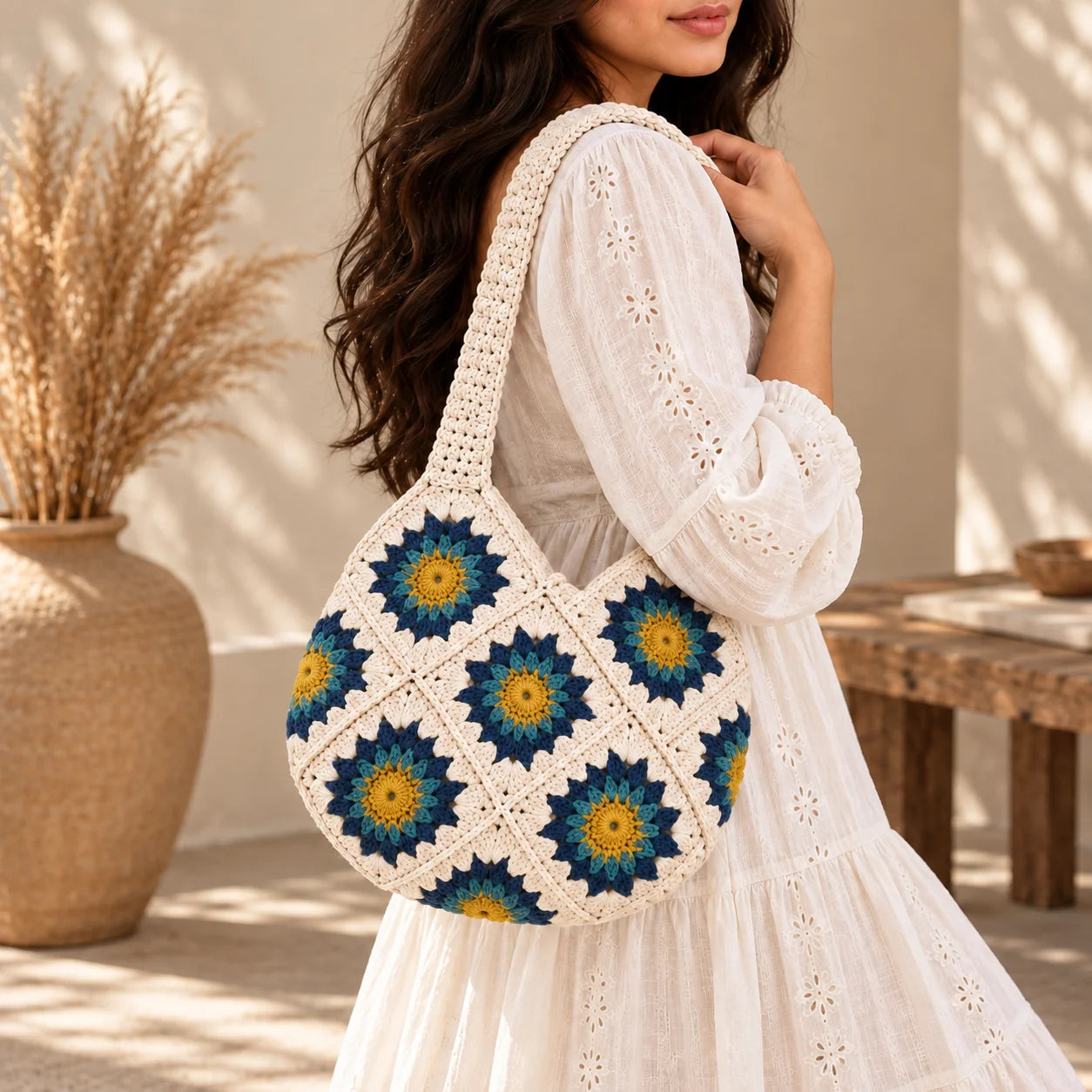"White crochet bag featuring
colourful floral granny-square patterns in blue, and yellow, with a textured handmade design and bohemian-inspired style."