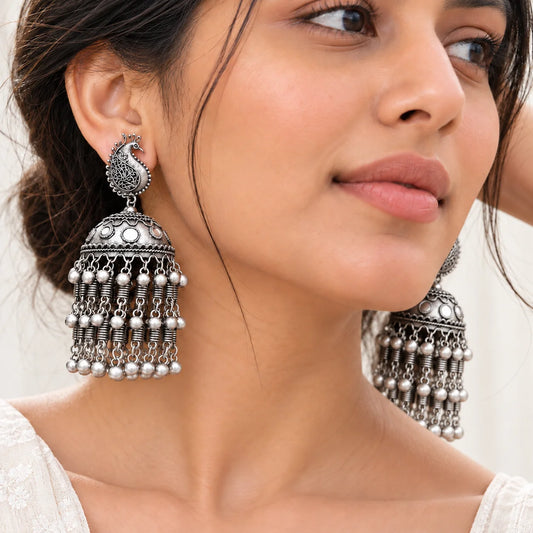 "Oxidised silver jhumka
earrings featuring intricate peacock-inspired motifs, engraved dome-shaped drops, and multiple rows of dangling silver accents in a traditional ethnic design."