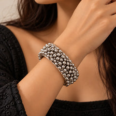 "Antique silver-tone
bangle featuring a wide, bold design with multiple rows of raised metallic beads and an intricate textured finish, showcasing a traditional ethnic style."