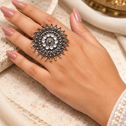 "Oxidised silver statement
ring featuring an intricate circular design, concentric embossed patterns, and decorative sunburst edges with delicate bead-like accents."