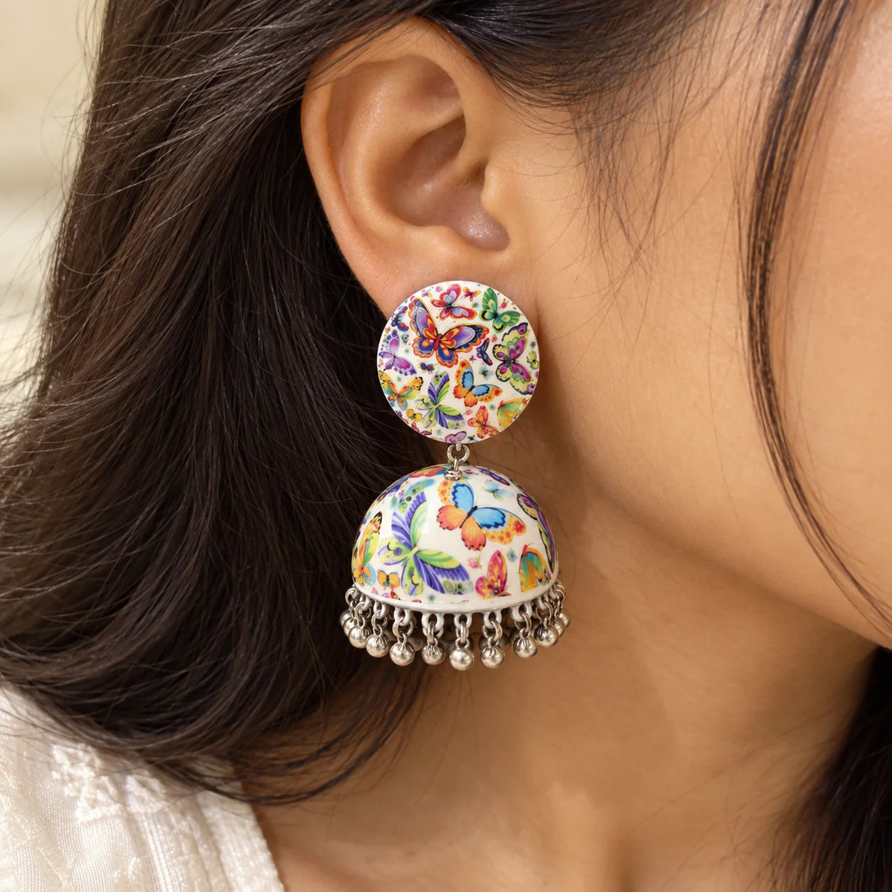White butterfly print jhumka earrings with multicolour butterfly patterns, dome-shaped drops, and silver-tone dangling charms.
