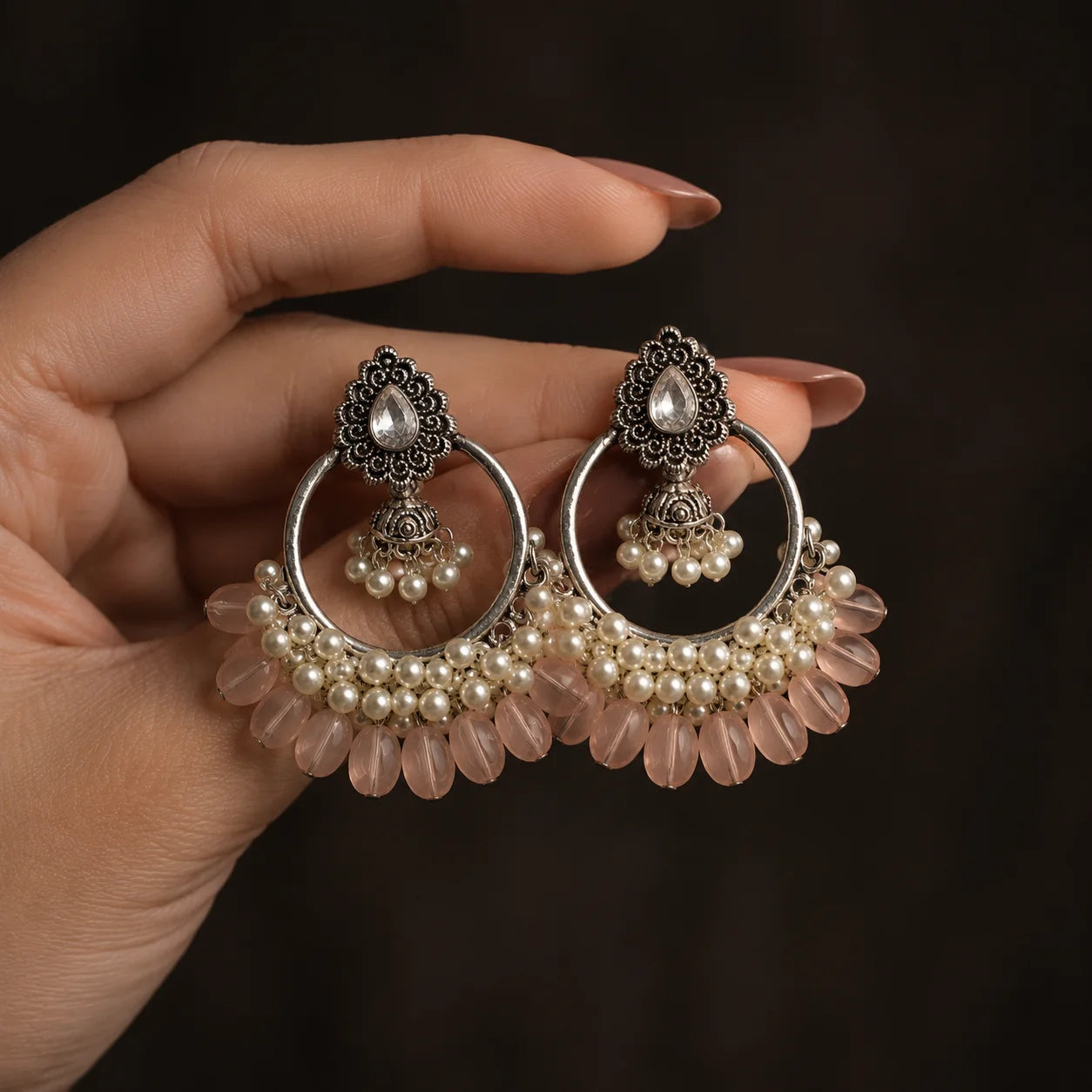 Silver plated chandbali jhumka earrings with baby pink beads and pearl clusters on wood. Traditional kundan stud earrings with hoop, mini jhumka, and pink bead drops for women. Festive wear silver tone chandbali earrings with white pearls and pastel pink detailing.