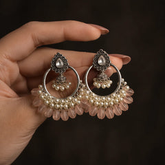 Silver plated chandbali jhumka earrings with baby pink beads and pearl clusters on wood. Traditional kundan stud earrings with hoop, mini jhumka, and pink bead drops for women. Festive wear silver tone chandbali earrings with white pearls and pastel pink detailing.