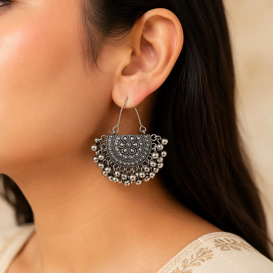"Oxidised silver-tone floral
earrings featuring intricate embossed detailing and multiple dangling ghungroo accents in a traditional statement design for women."