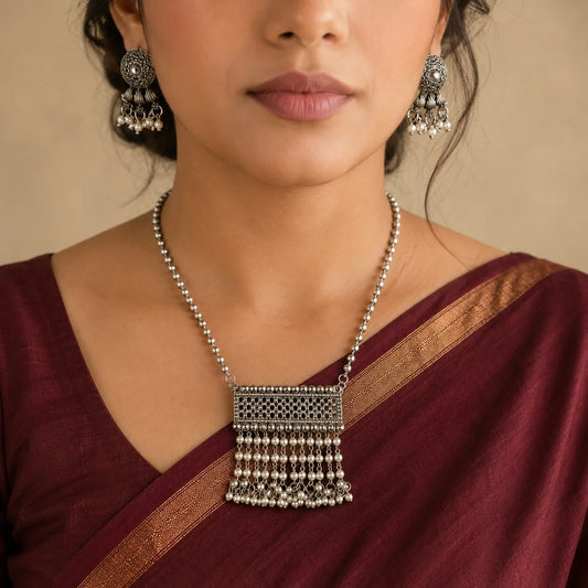 "Oxidised silver-tone jewellery
set featuring a statement necklace with intricate detailing, white pearl drops and matching ethnic earrings."