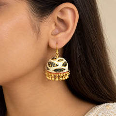 "Pair of ivory-white
dome-shaped jhumka earrings featuring bold black leaf motifs with golden detailing and a fringe of gold-tone bead danglers."
