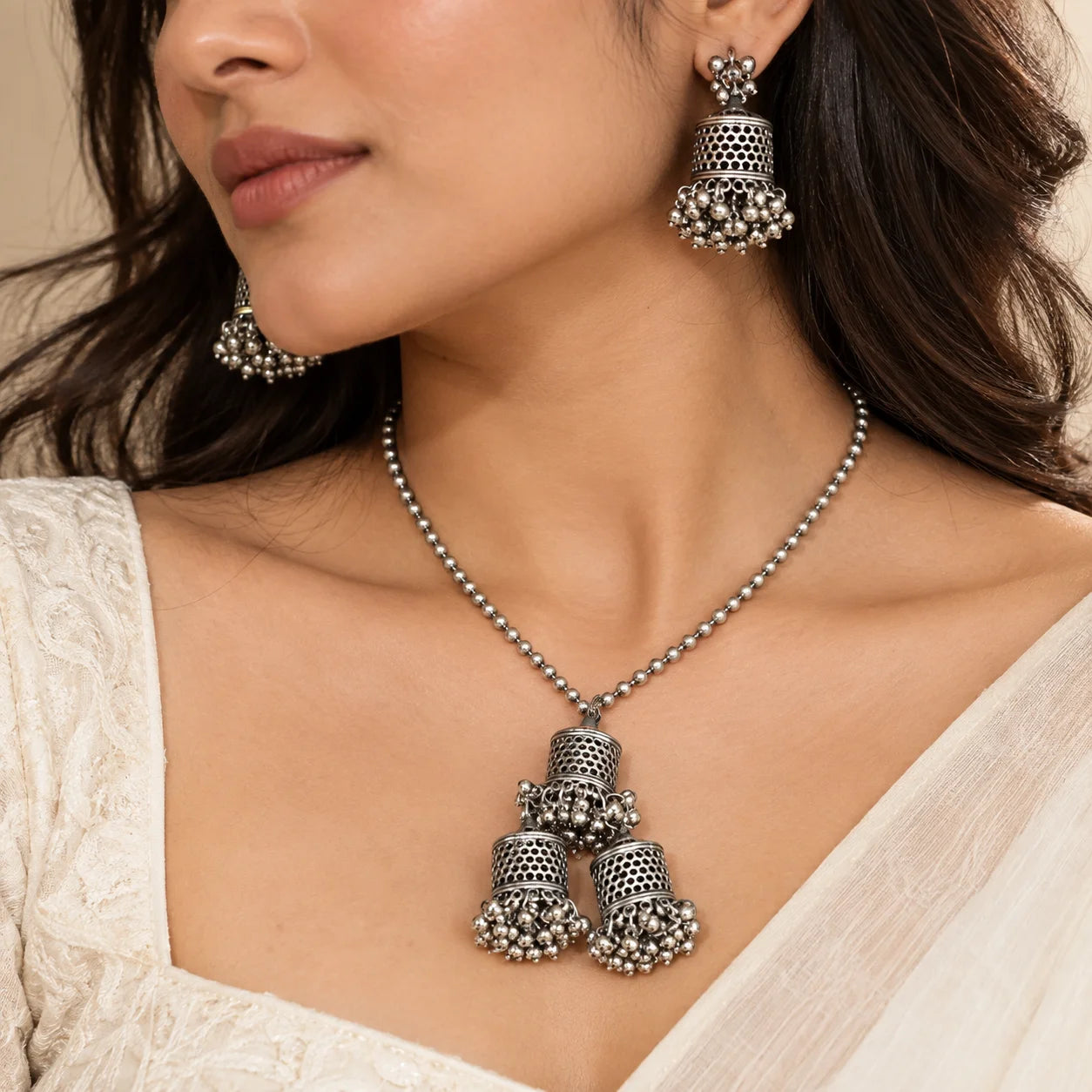 "Silver-toned necklace
set featuring a beaded chain, a cluster of intricately detailed jhumka-style bell pendants with dangling bead accents, and matching jhumka earrings."