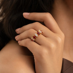 Gold open cuff ring with ruby red marquise crystals on wooden table. Adjustable gold-tone ring featuring red stones and ball-end tips.