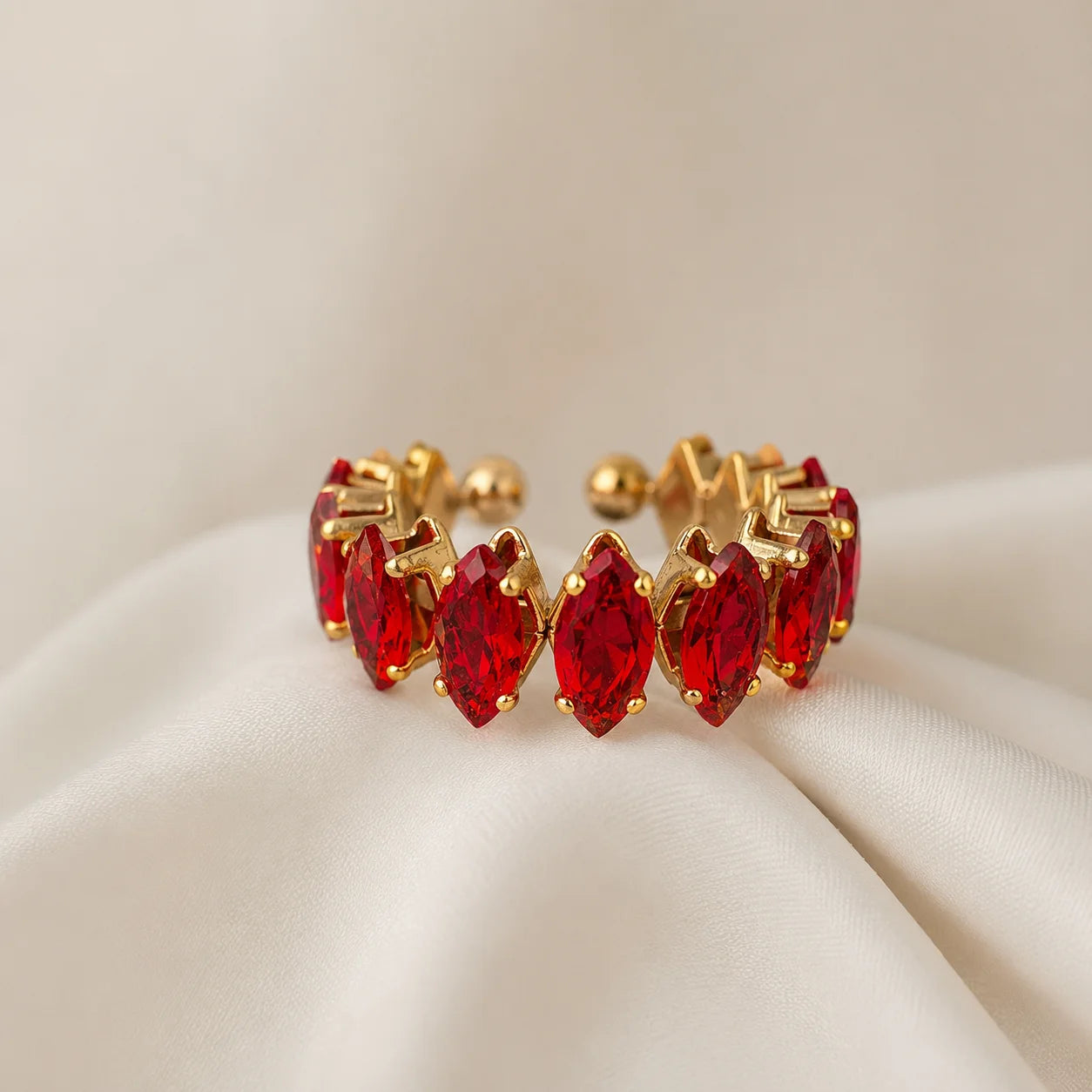 Gold open cuff ring with ruby red marquise crystals on wooden table. Adjustable gold-tone ring featuring red stones and ball-end tips.