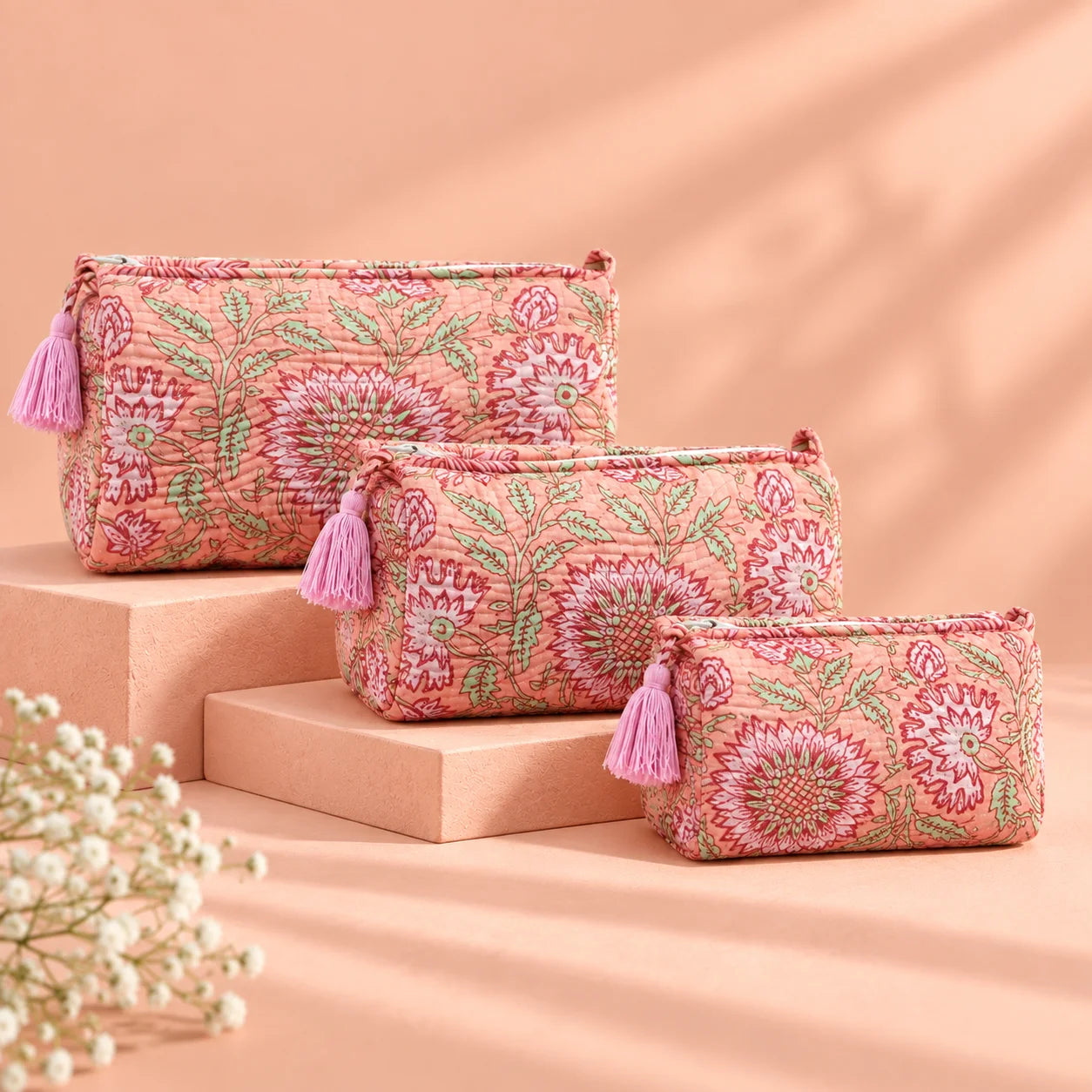 "Set of three peach
fabric pouches featuring intricate floral and leafy prints in burgundy, rose, and green, arranged in different sizes."