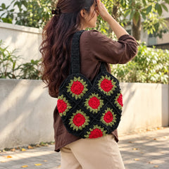 "Handcrafted black crochet
bag featuring bold red floral motifs with olive-green leaf detailing and sturdy crochet handles."