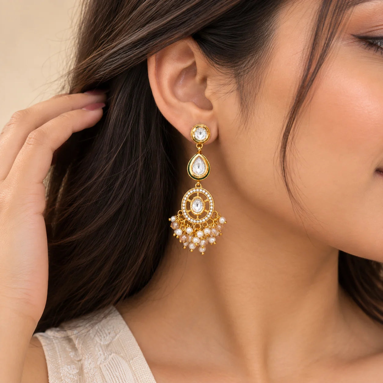 "Gold-tone statement earrings
featuring green-bordered teardrop stones, circular kundan-style detailing, and dangling white pearls with translucent beads."