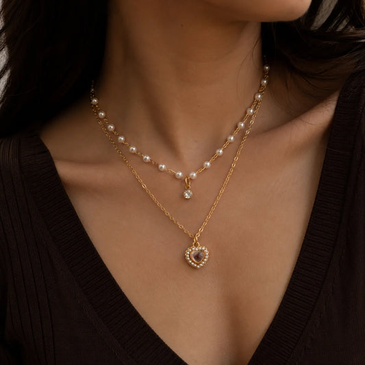 "Gold-tone layered pearl necklace featuring delicate
faux pearls, a vintage-inspired heart pendant with
pearl detailing, and a dainty crystal charm. Elegant
women's fashion jewellery for everyday wear,
parties, and special occasions."