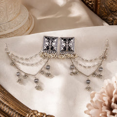 Oxidized silver earchain earrings with square floral studs, layered pearl chains, and jhumka-style danglers arranged on a wooden surface.
