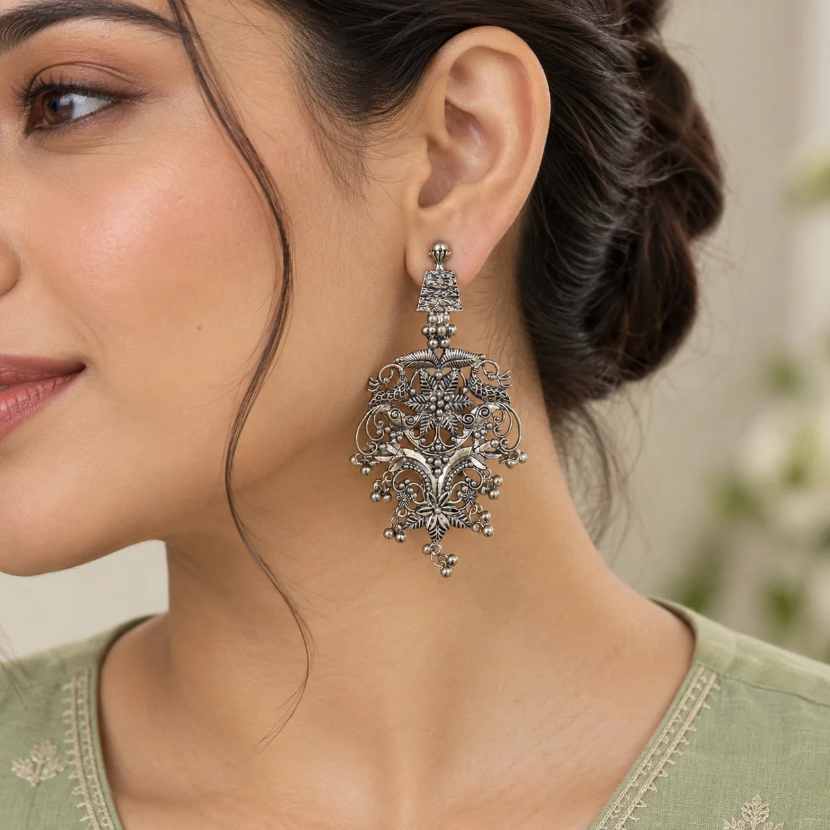 "Silver statement
 earrings featuring layered floral motifs, intricate filigree detailing, curved traditional patterns, and delicate dangling bead accents."
