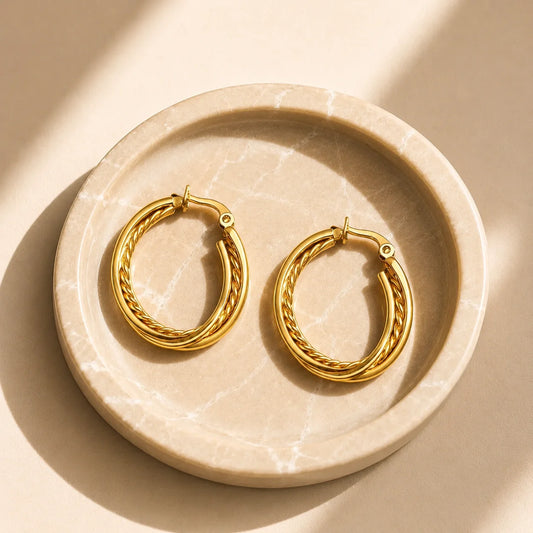 Hand holding gold triple layer hoop earrings with braided chain detail. Large gold-tone hoop earrings featuring three rows and rope texture center.
