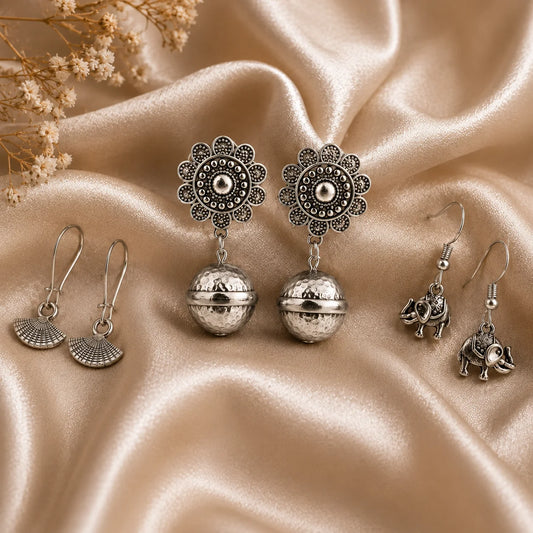 Set of 3 oxidised silver earring pairs. Elephant hook earrings, fan-shaped hooks, and floral jhumkas with ball drops. Antique silver ethnic combo.
