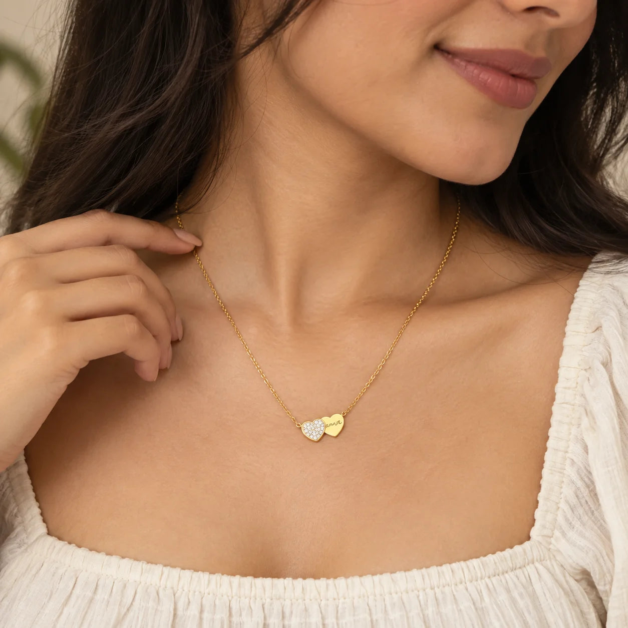 "Delicate gold-tone necklace
 featuring two overlapping heart pendants, one embellished with sparkling stones and the other with a polished gold finish, displayed on a dark background."
