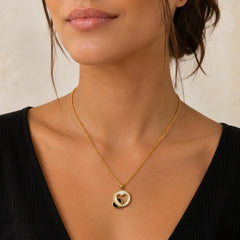 "Gold-tone necklace
 with a delicate chain and an intertwined double-heart pendant, displayed on a wooden surface."
