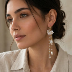 Pair of gold-tone statement earrings featuring delicate white floral charms, cascading chains, crystal-like accents, and lustrous pearl drops.
