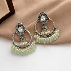 "Silver plated chandbali jhumka earrings with mint green beads and pearl clusters on wood.
Traditional kundan stud earrings with hoop, mini jhumka, and pearl drops for women.
Festive wear silver tone chandbali earrings with white pearls and mint bead detailing."
