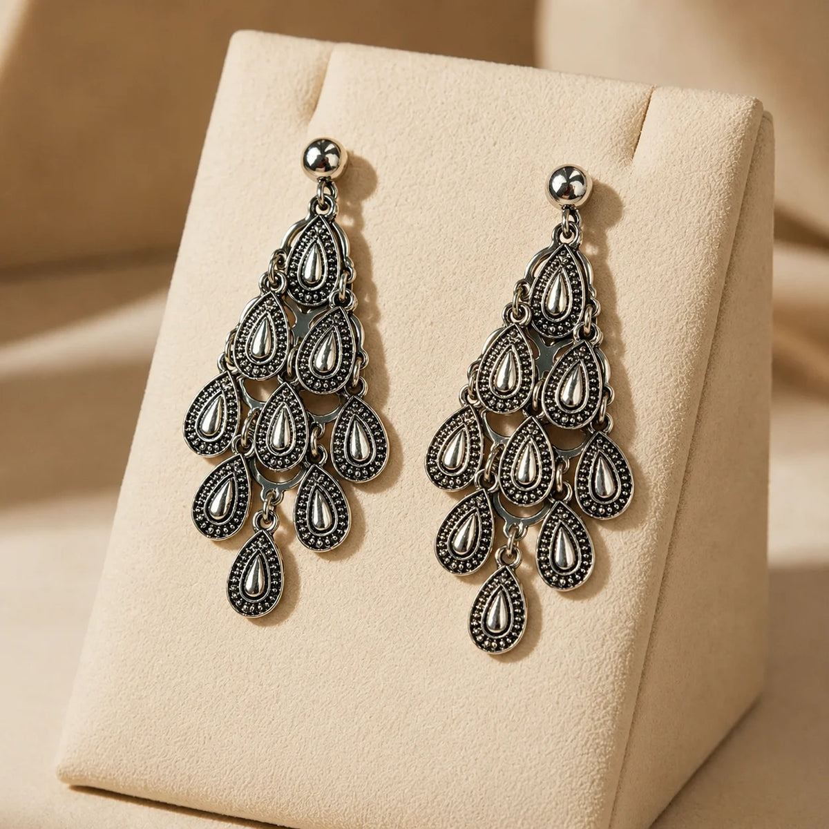 Antique silver chandelier dangle earrings with tiered teardrop motifs on wood surface. Ethnic fusion raindrop chandelier earrings with antique finish and push back post for women.


