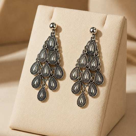 Antique silver chandelier dangle earrings with tiered teardrop motifs on wood surface. Ethnic fusion raindrop chandelier earrings with antique finish and push back post for women.

