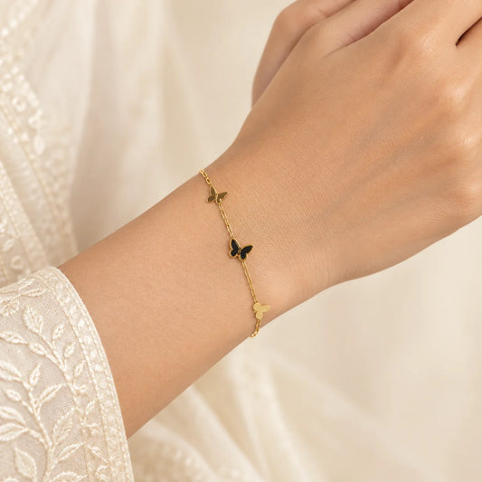 "Gold-tone delicate chain 
bracelet featuring three butterfly charms, including a central dark enamel butterfly, with an adjustable extension chain."
