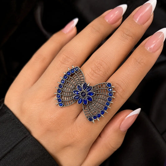 "Oxidised silver-tone 
statement ring featuring a butterfly-inspired design with vibrant blue accents, intricate detailing and a floral centre."
