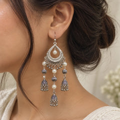 "Silver-toned statement
 jhumka earrings with intricate teardrop motifs, white pearl accents, textured beads, and multiple cascading bell-shaped charms."
