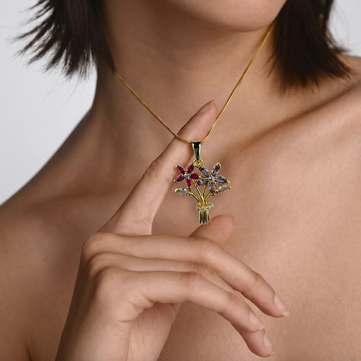 Feminine gold flower bunch necklace with multi-color crystal stones and a crystal-studded bow detail. Features two detailed blooms in pink and purple with clear stone accents for sparkle. Lightweight 18K gold plated brass makes it comfortable for daily wear.
