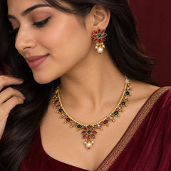 Ruby green kundan necklace set with gold-toned detailing, multicolor stones, pearl drops, and matching floral earrings.
