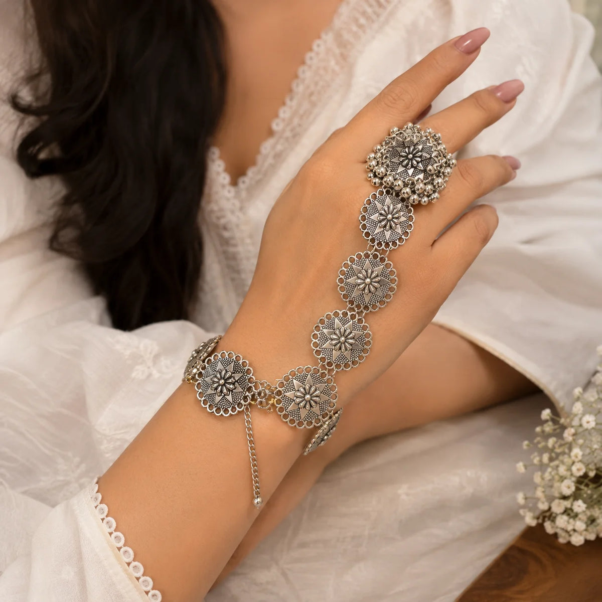 "Oxidised silver-tone 
hathphool for women featuring intricate floral medallions, traditional detailing, and ghungroo accents connected from finger to wrist."

