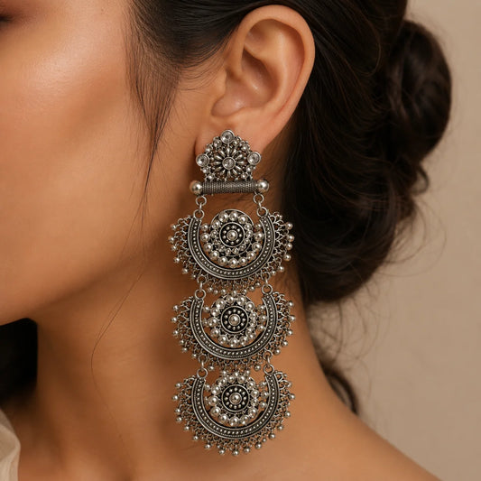 "Triple-layered oxidised
 silver-tone chandbali earrings with intricate circular motifs, mirror-style accents, and traditional ghungroo detailing for women."
